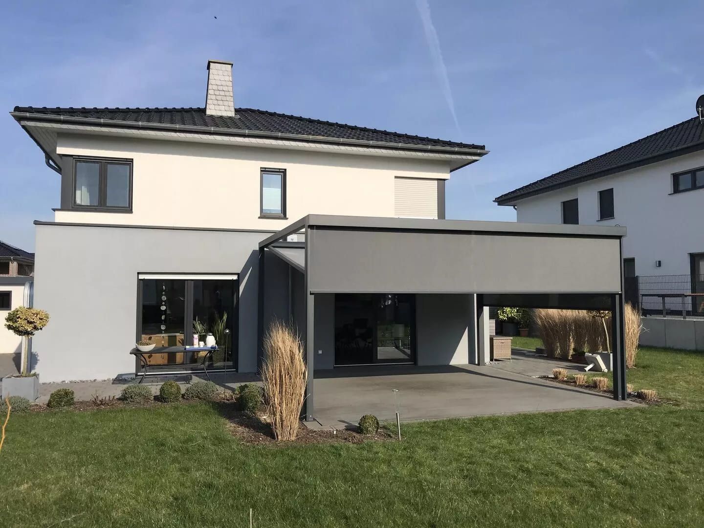 Ein modernes zweistöckiges Haus mit einem schlichten grauen Innenhof, grünem Rasen und einem klaren blauen Himmel im Hintergrund.