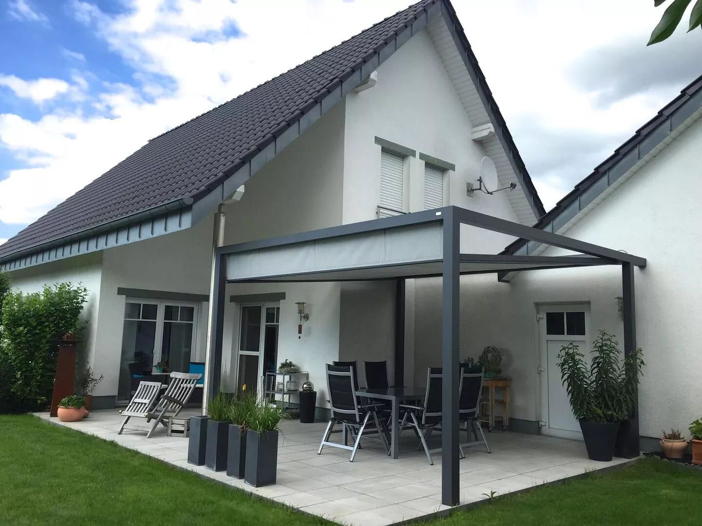 Modernes Haus mit einer überdachten Terrasse mit Essmöbeln, üppigem Gras und einem klaren Himmel im Hintergrund.